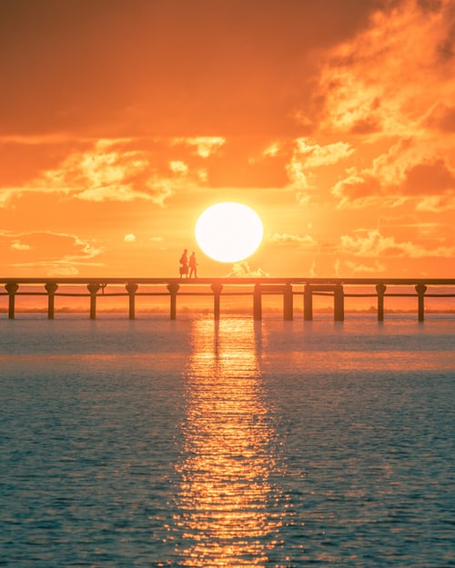 Two people walking across a bridge at sunrise to symbolise the importance of phoning people early in the morning or late at night