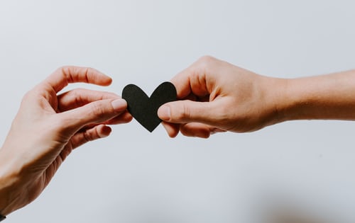 Two hands holding a black heart cut out to exchange