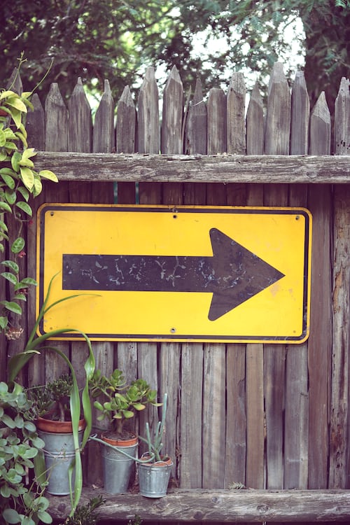 A right run road sign on a garden fence surrounded by shrubs and trees