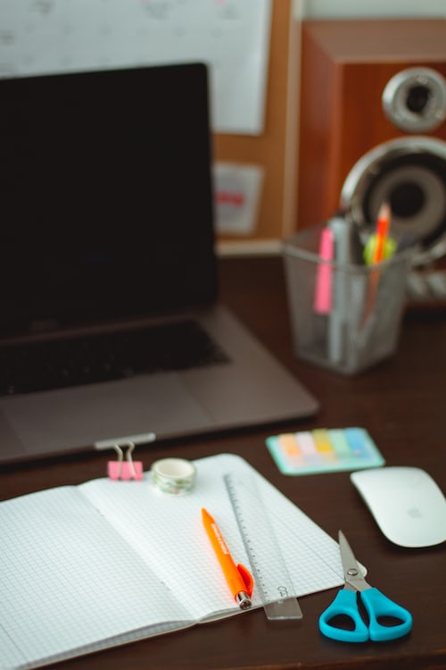 An exercise work book and stationary resting in front of a laptop