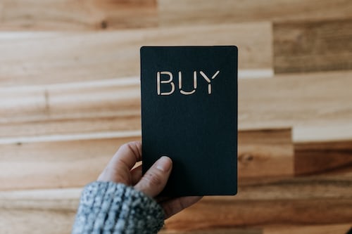 A person holding a black card with the word buy carved into it